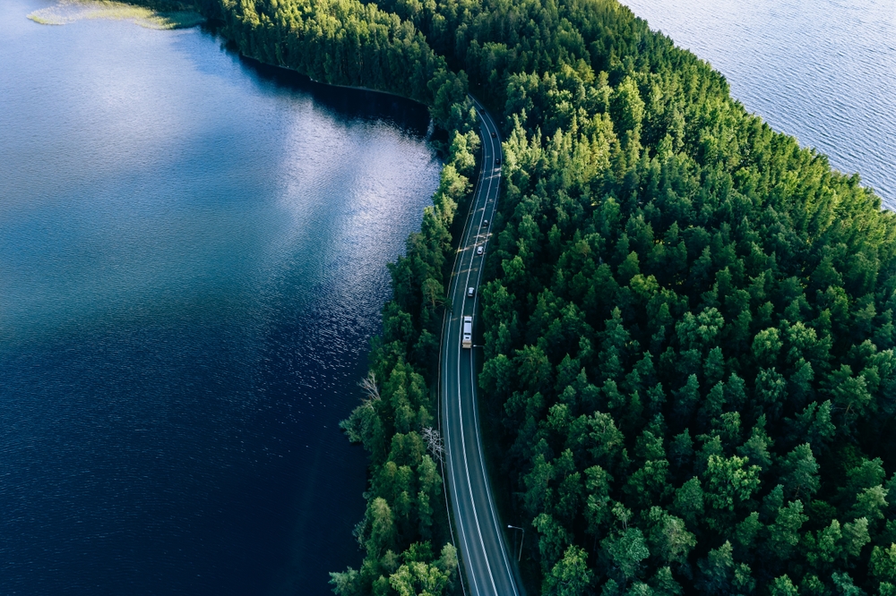 An aerial photo of a road running through a forest, next to a lake